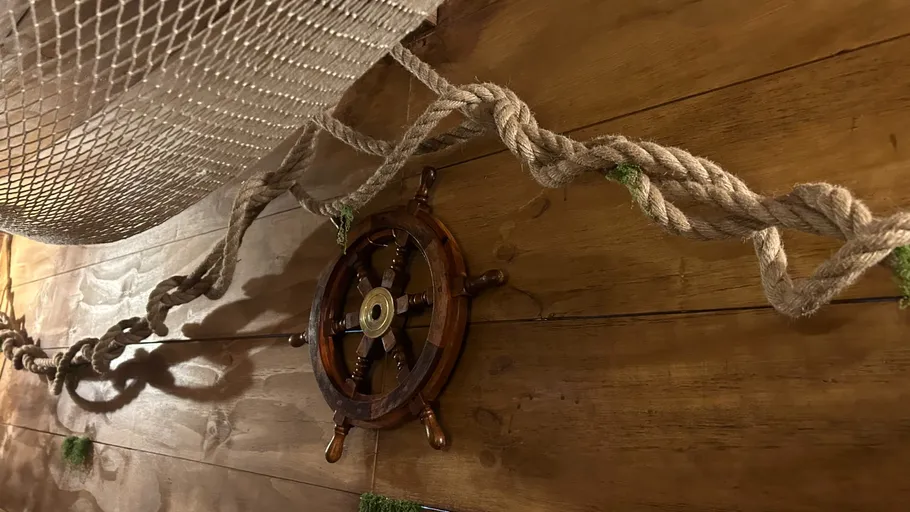 Steuerrad an Holzwand mit Seildekoration.