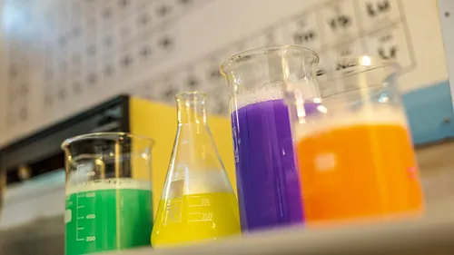 Bunte Flüssigkeiten in Bechern und Kolben, Laborhintergrund.