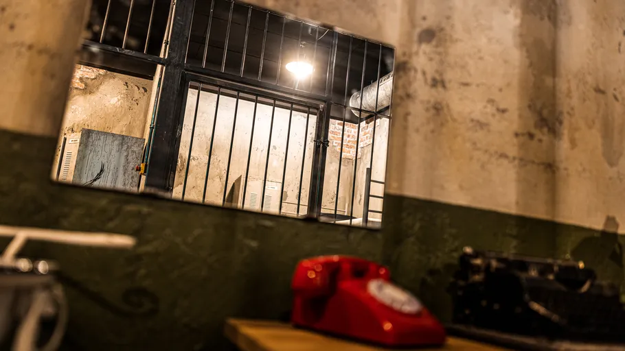 Rotes Telefon, Tisch, vergittertes Fenster, dunkler Raum.