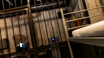 Prison cell with metal bars and bed.