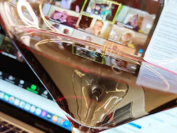 Eine Weinglas spiegelt Videokonferenz-Teilnehmer auf Laptop-Bildschirm.