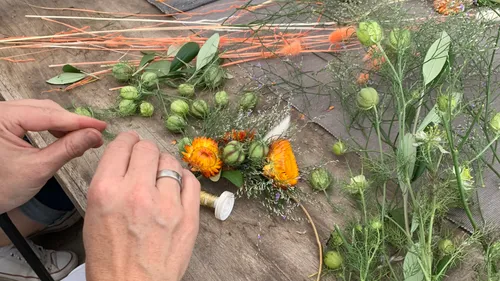 Hands crafting floral arrangement on wooden table.