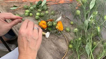 Hands crafting floral wreath on wooden table.