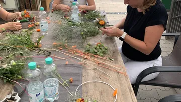 Women crafting flower arrangements at outdoor table.