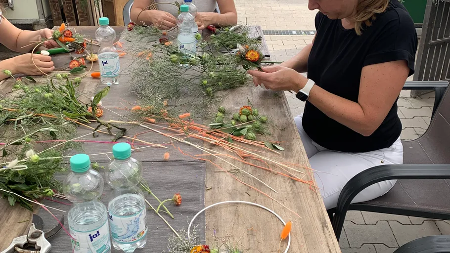 Women crafting flower arrangements at outdoor table.