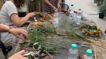 Personen arrangieren Blumen auf einem Holztisch im Freien.