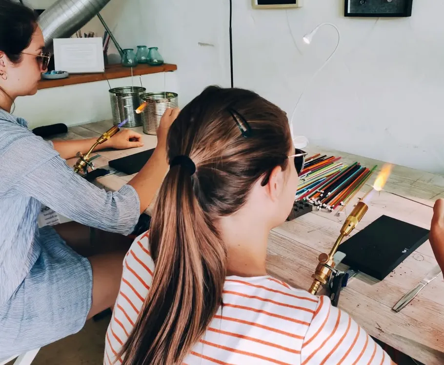 Two women crafting with glass torches on table.