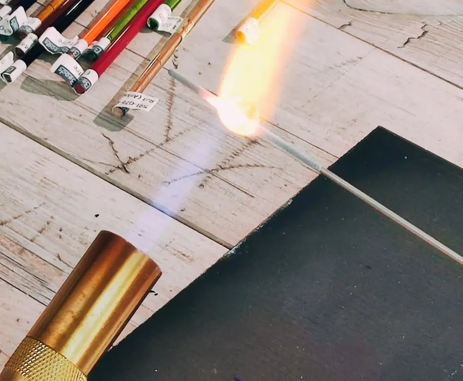 Lötlampe erhitzt Metallstab auf Holztisch.