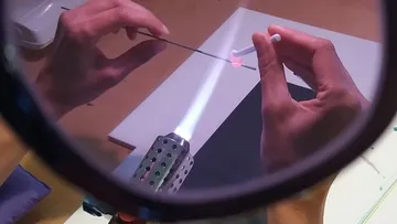 Hände formen Glas über Flamme, vergrößerte Ansicht.