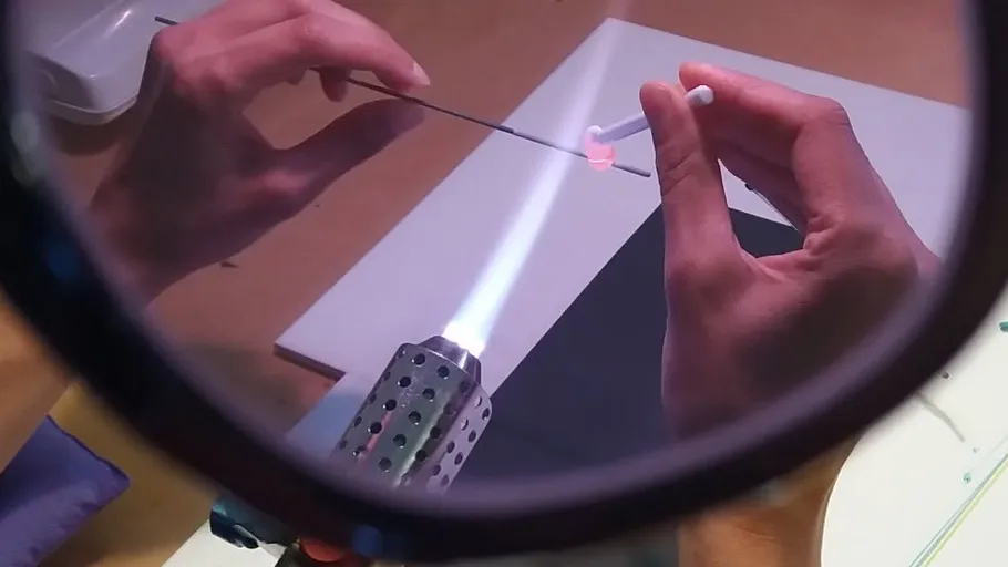 Hands shaping glass over a flame, magnified view.