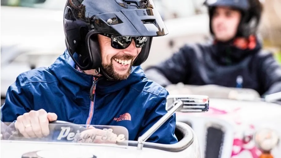 Mann mit Helm fährt einen altmodischen Wagen.