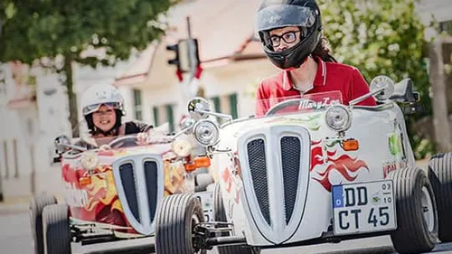 Zwei Personen fahren kleine Oldtimer-Autos im Freien.