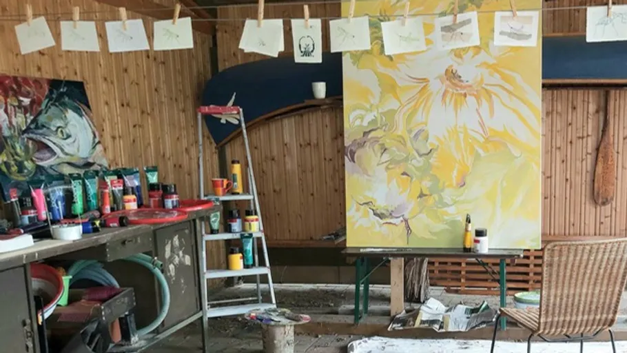 Art studio with paintings and supplies on shelves.