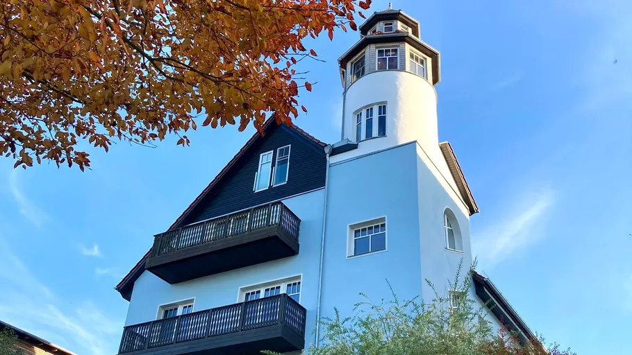 Großes Haus mit Turm, Herbstblätter, blauer Himmel.
