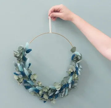 Hand hält Blumenkranz vor blauer Wand.