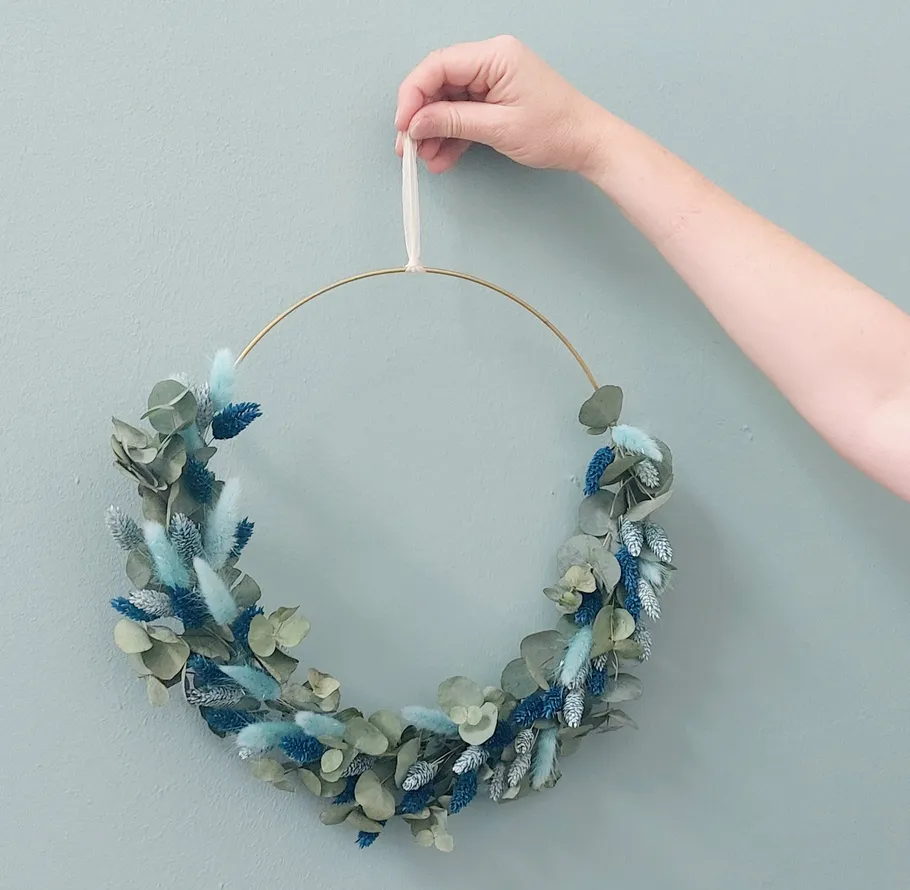 Hand hält Blumenkranz vor blauer Wand.