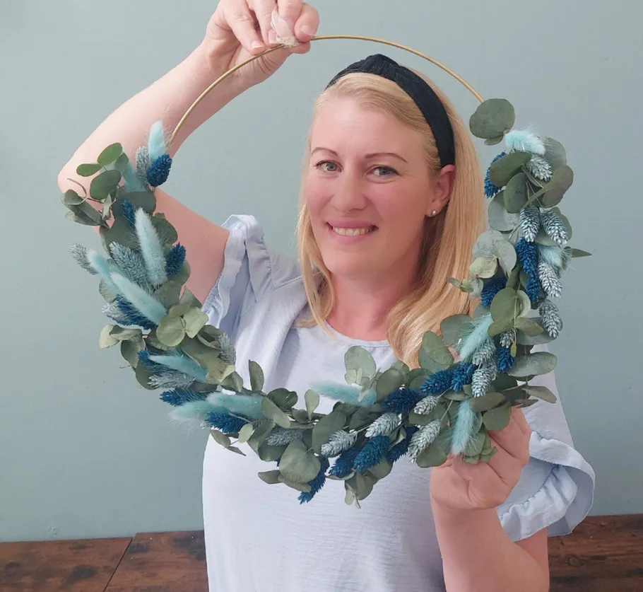 Woman holding decorative wreath with blue accents indoors.