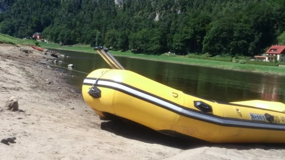 Gelbes Schlauchboot am Flussufer, Wald im Hintergrund.