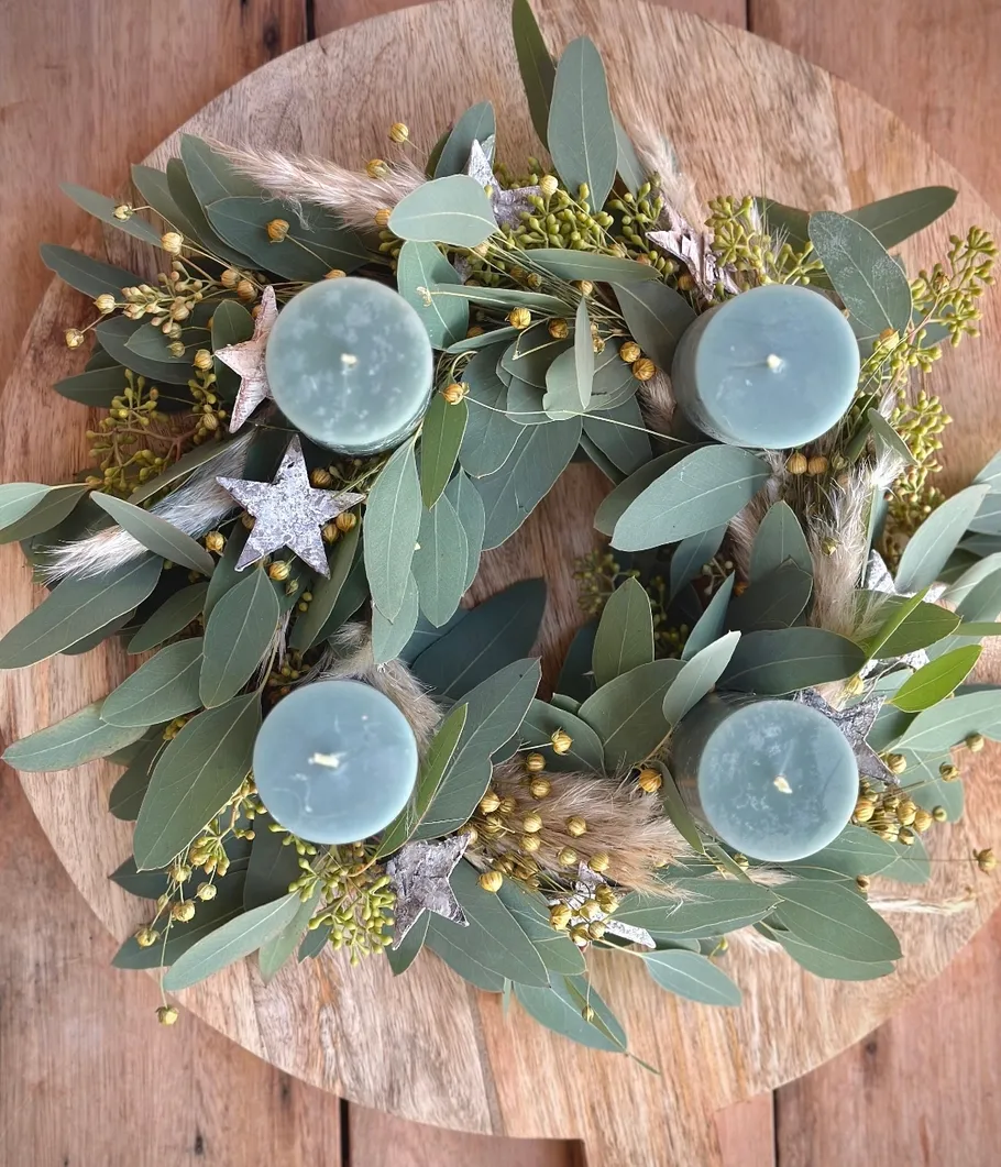 Green candles on leafy wreath, wooden table.