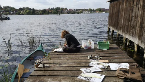 Person painting on dock by a lake.