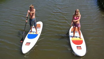 Two people paddleboarding on a calm river.