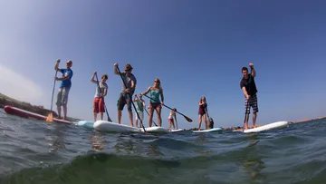 Group paddleboarding on calm water under clear sky.