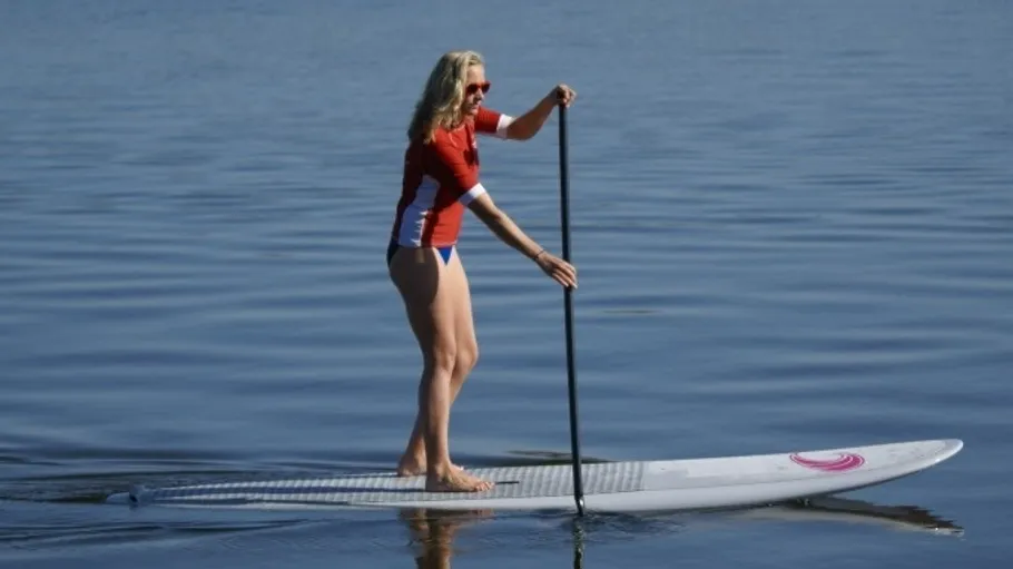 Woman paddleboarding on calm water surface.