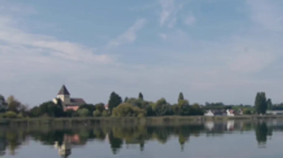 Kirche neben See unter blauem Himmel.