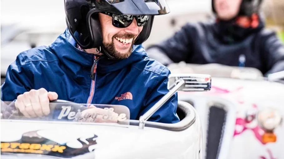 Man driving small car, smiling, wearing helmet.