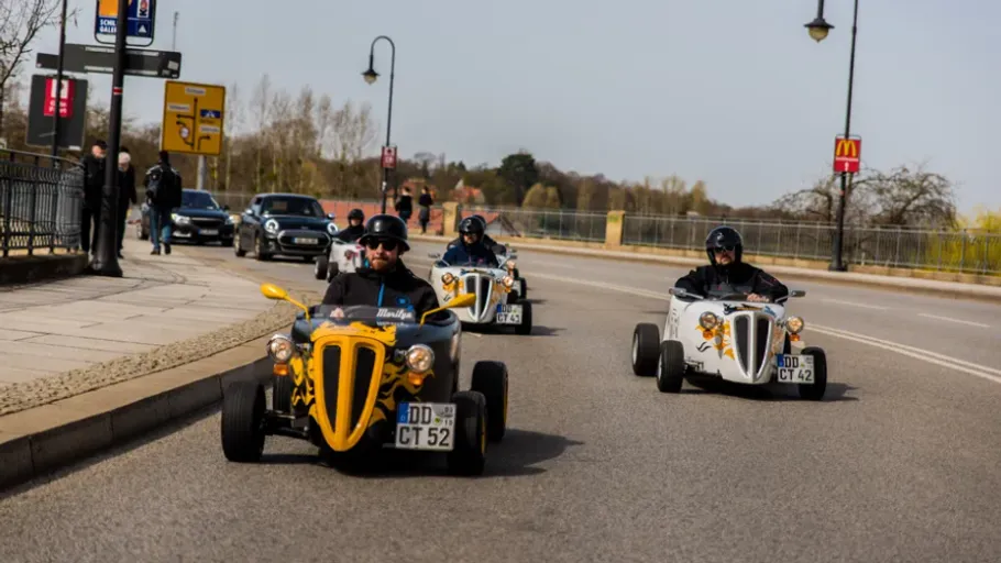 Three people driving motorized trikes on road.