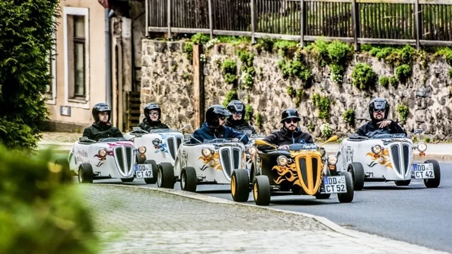 Group driving mini hot rods on a street.