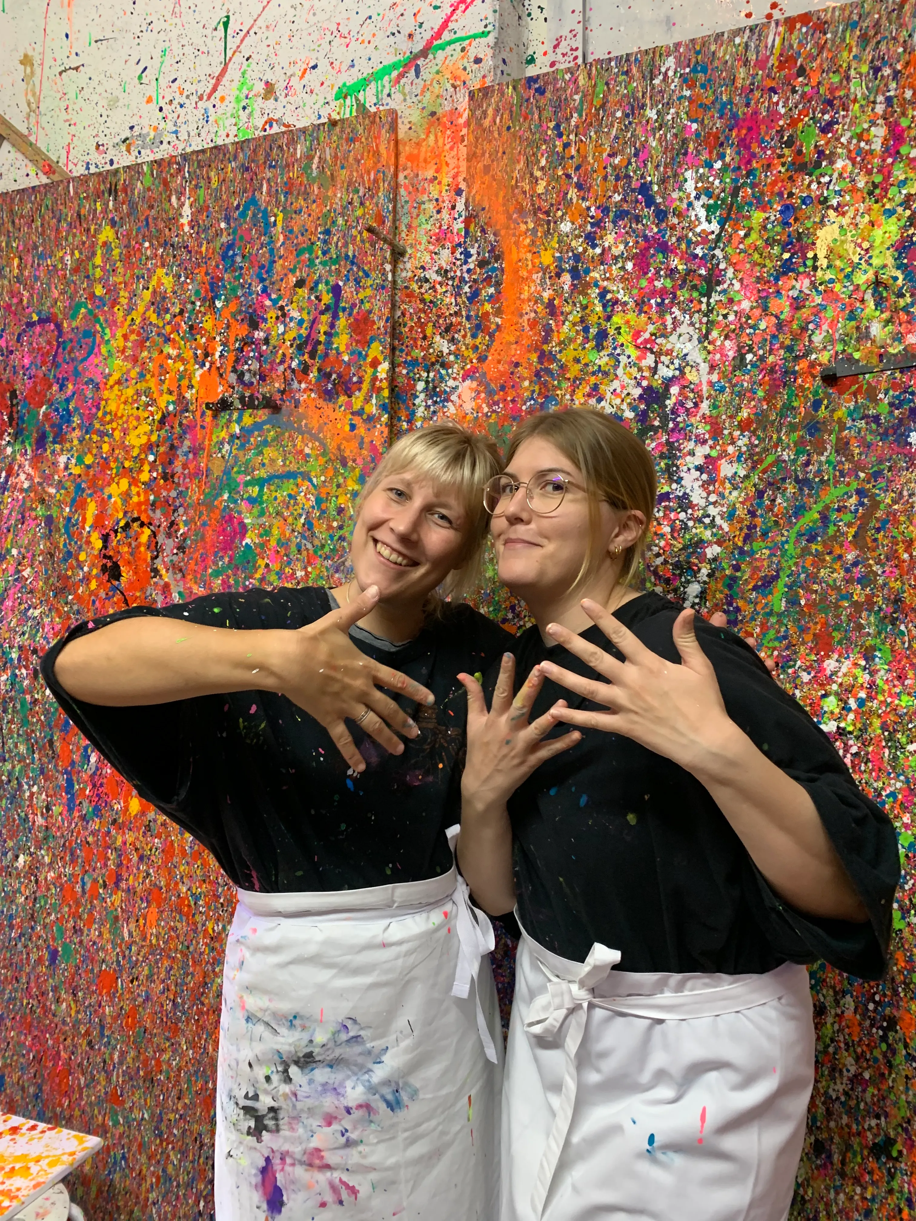 Two women pose in front of colorful splatter art.