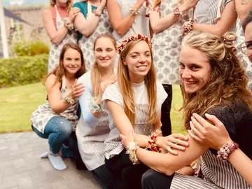 Women wear aprons, smile, and interact outdoors.