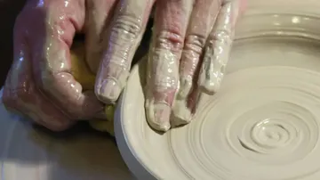 Hands sculpting clay on potter's wheel.