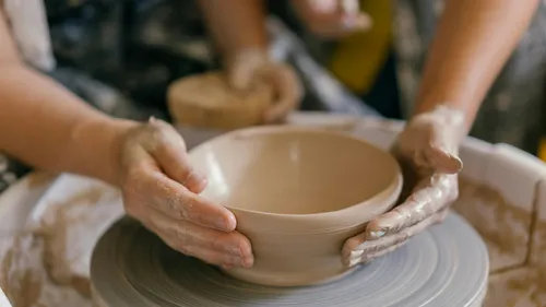 Hands shaping pottery on a spinning wheel.