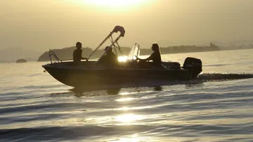 Boot mit Menschen auf ruhigem Wasser bei Sonnenuntergang.