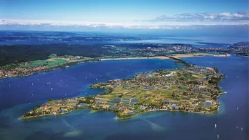 Lush island surrounded by blue lake, aerial view.