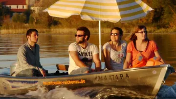 Vier Personen auf Boot mit gestreiftem Sonnenschirm.