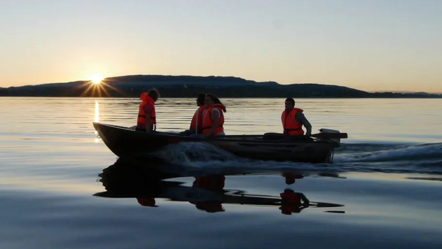 Boat with people at sunset on calm water.