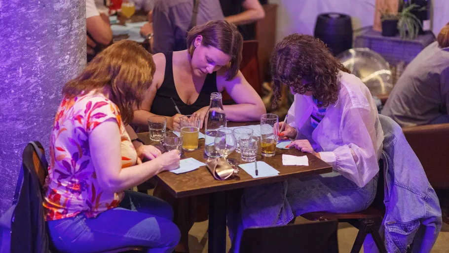 Drei Frauen schreiben an einem Kneipentisch.
