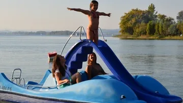 Kind steht auf Tretboot-Rutsche, zwei Frauen sitzen.
