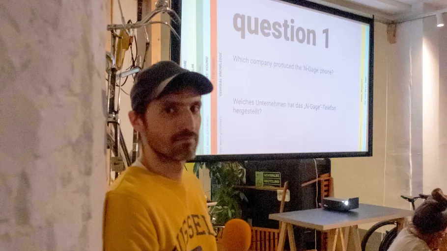 Mann mit Kappe neben Quizfrageprojektion im Raum.
