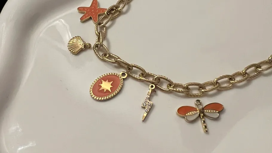 Gold charm bracelet with various pendants on plate.