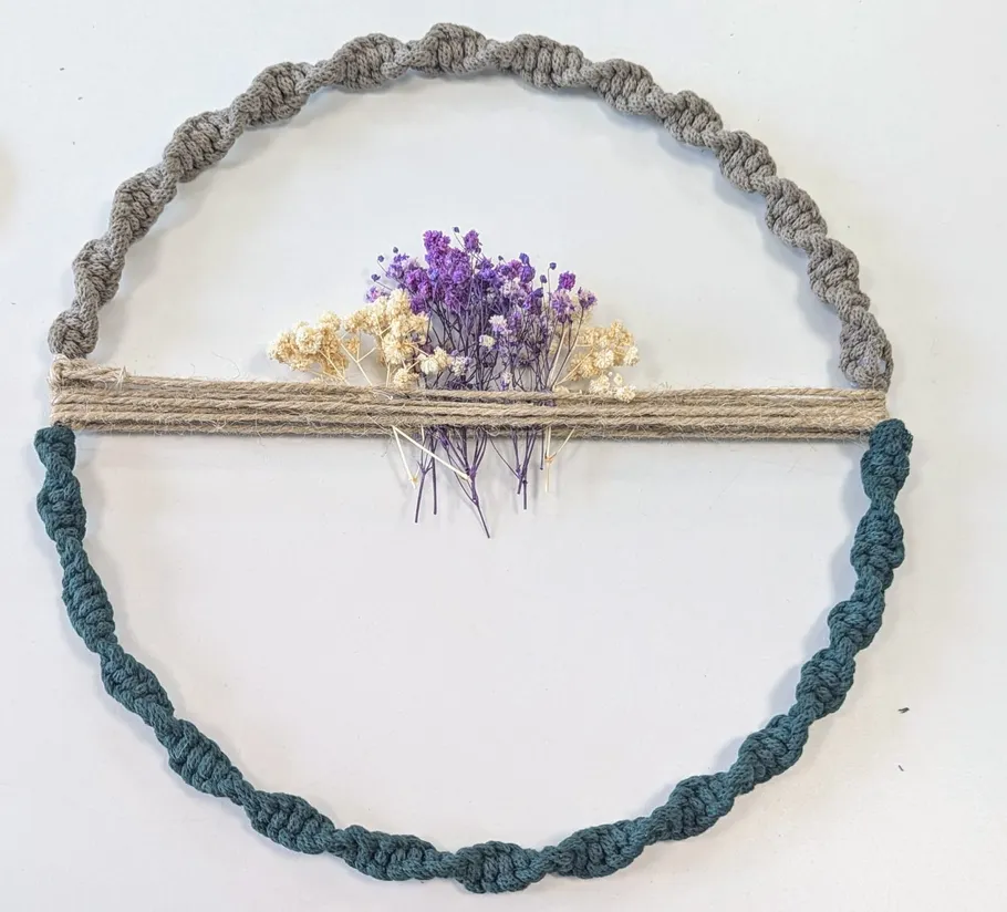 Makramee-Kreis mit Blumen auf weißem Hintergrund.