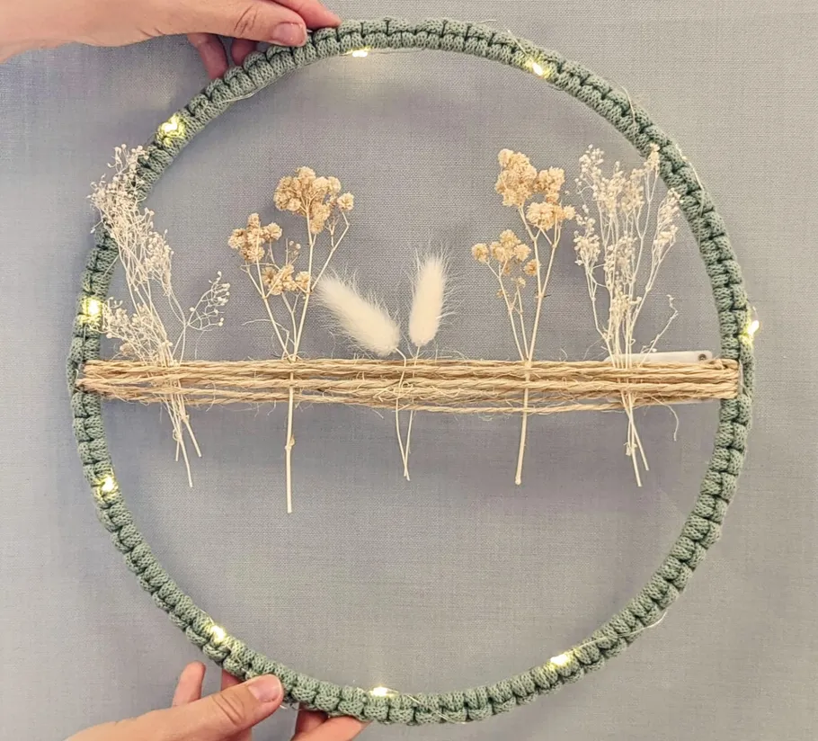 Hands holding decorated hoop with dried flowers.