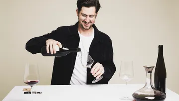 Man pouring wine into glass on table.