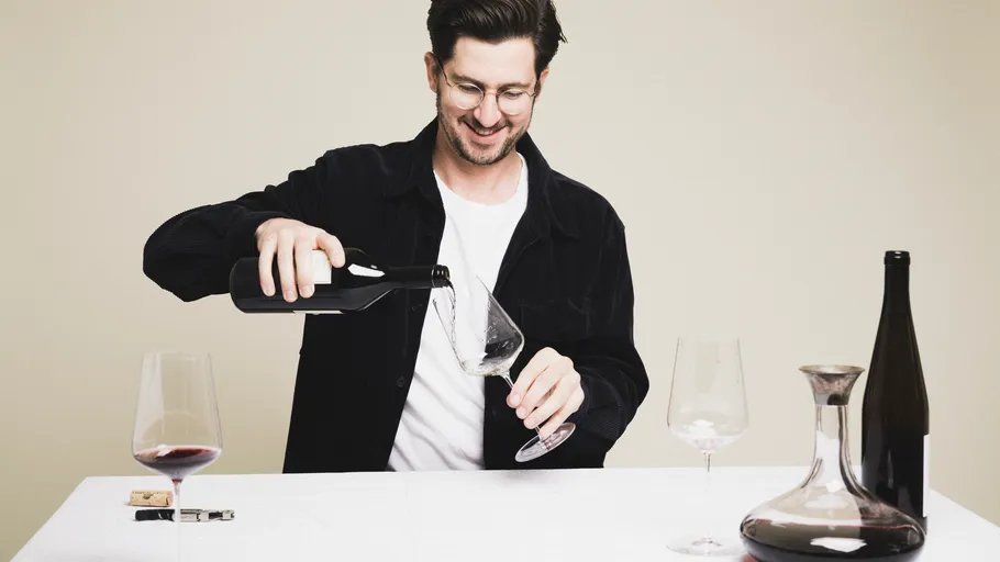 Mann gießt Wein in Glas auf Tisch.