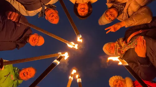 Gruppe hält Fackeln, lächelt bei Dämmerung.