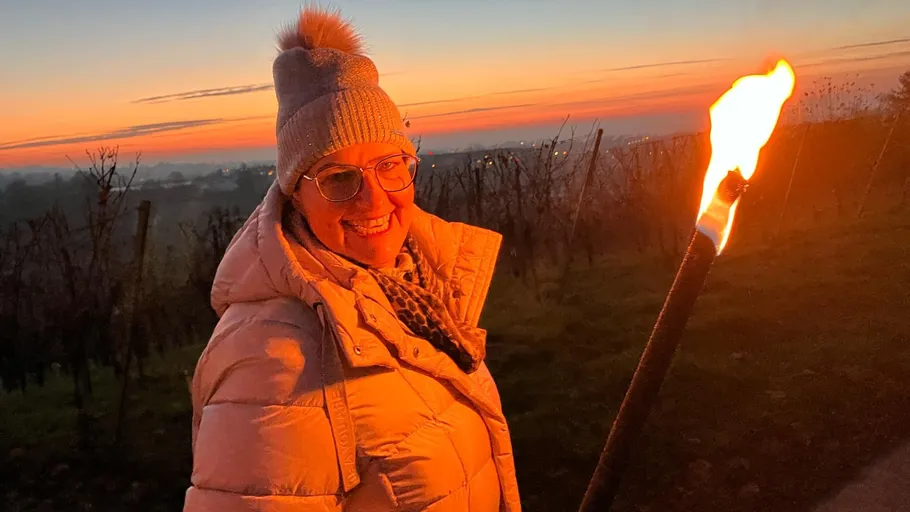 Person hält Fackel im Weinberg bei Sonnenuntergang.