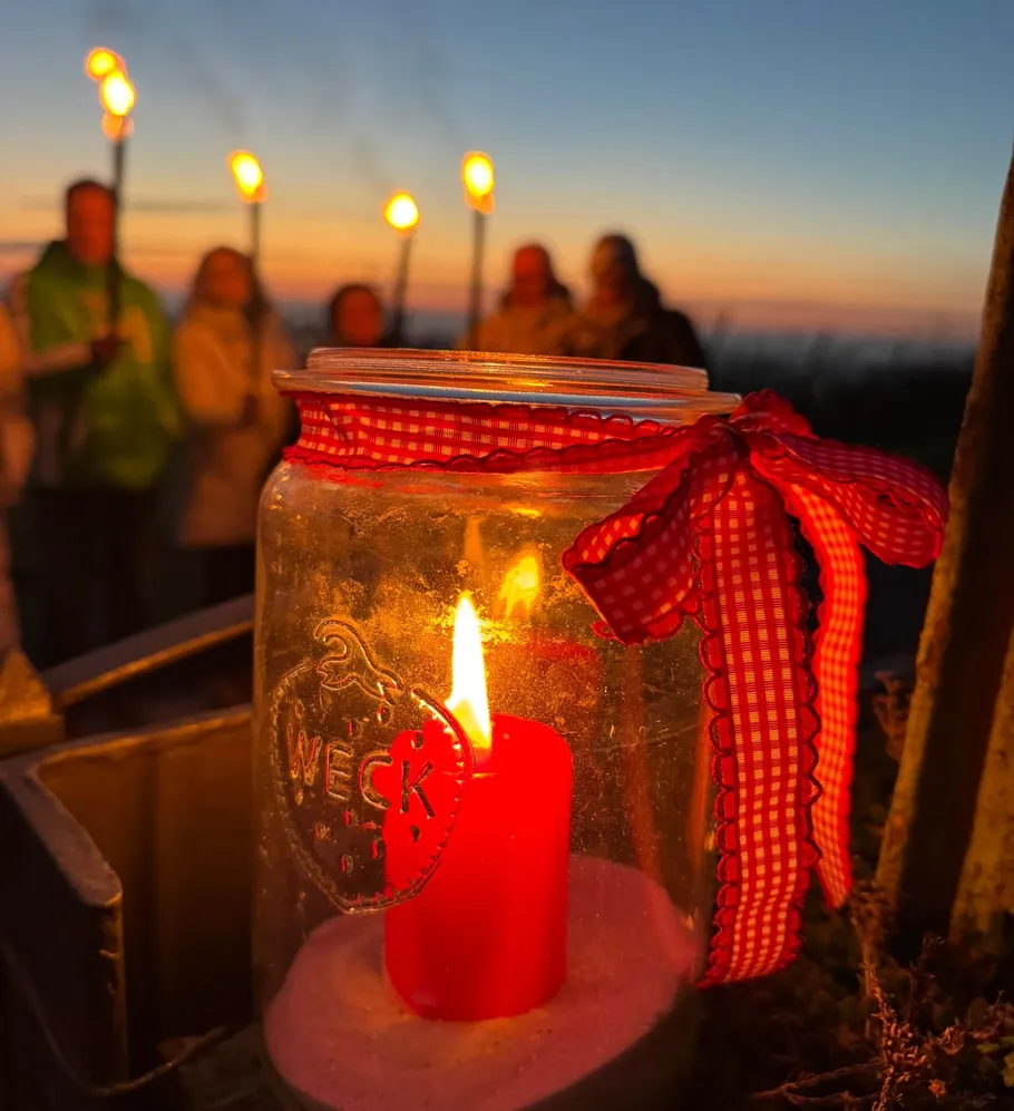Rote Kerze im Glas bei Sonnenuntergang, Menschen mit Fackeln.